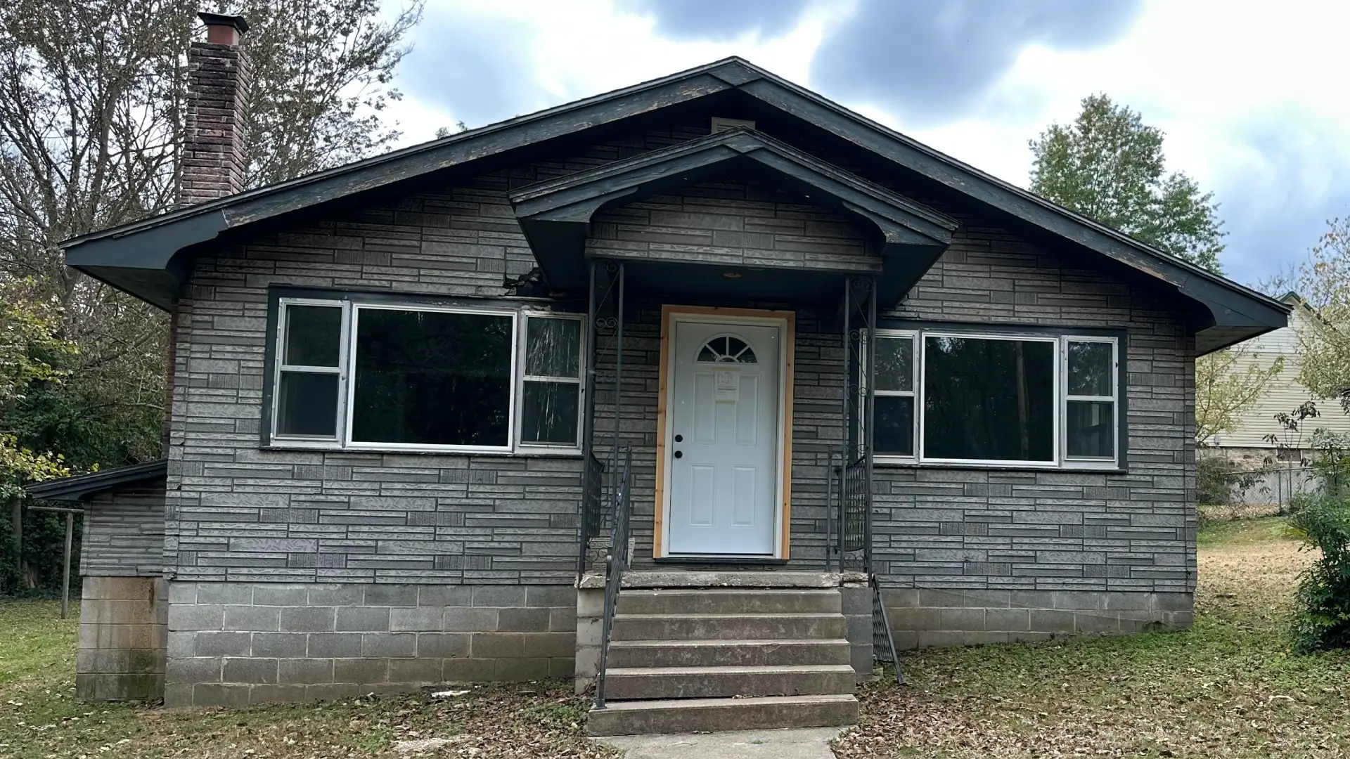 Exterior of a grey residential home with white-framed windows and a central front door.